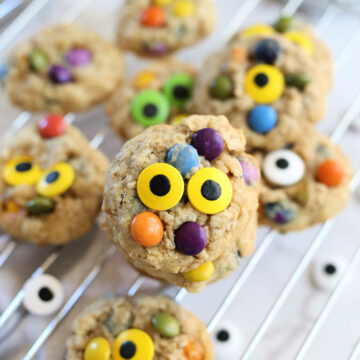 healthy monster cookies with yellow and green candy eyes on a cooling rack with a dish towel