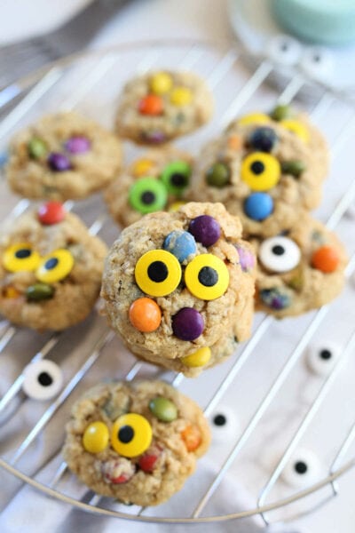 healthy monster cookies with yellow and green candy eyes on a cooling rack with a dish towel