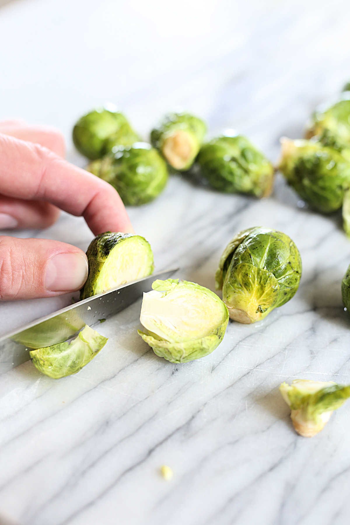 hand holding knife showing how to cut in half brussels sprouts