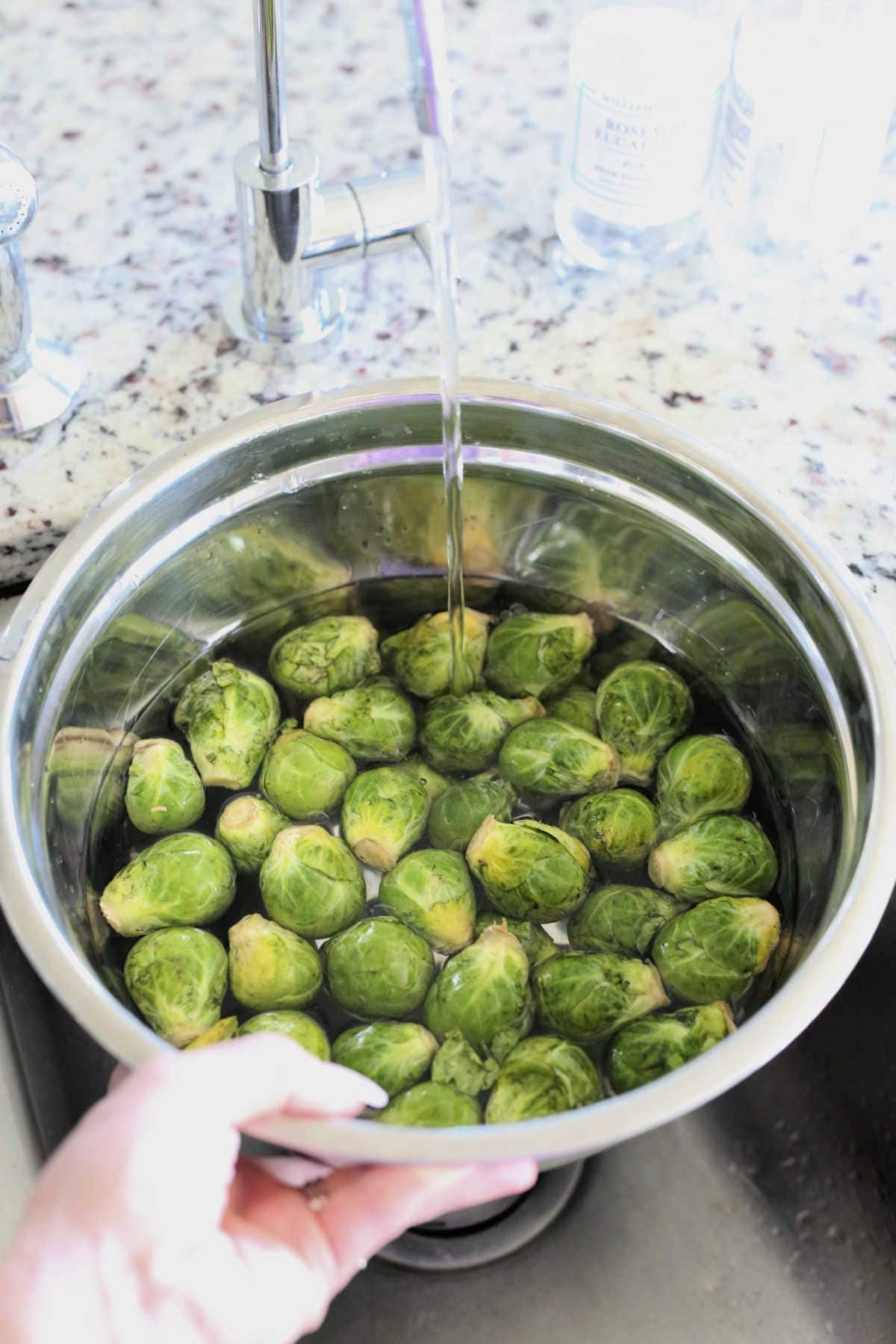 rinsing brussels sprouts in a colander in the sink to prepare for cutting