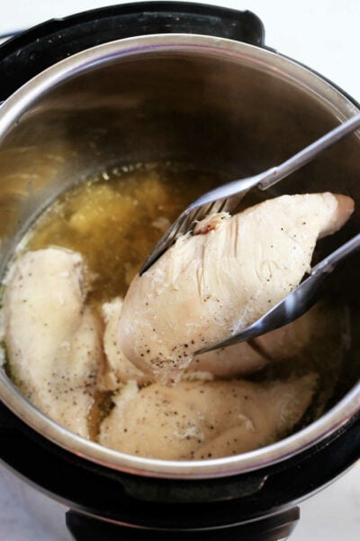 crockpot chicken breast lifted out of the slow cooker with tongs