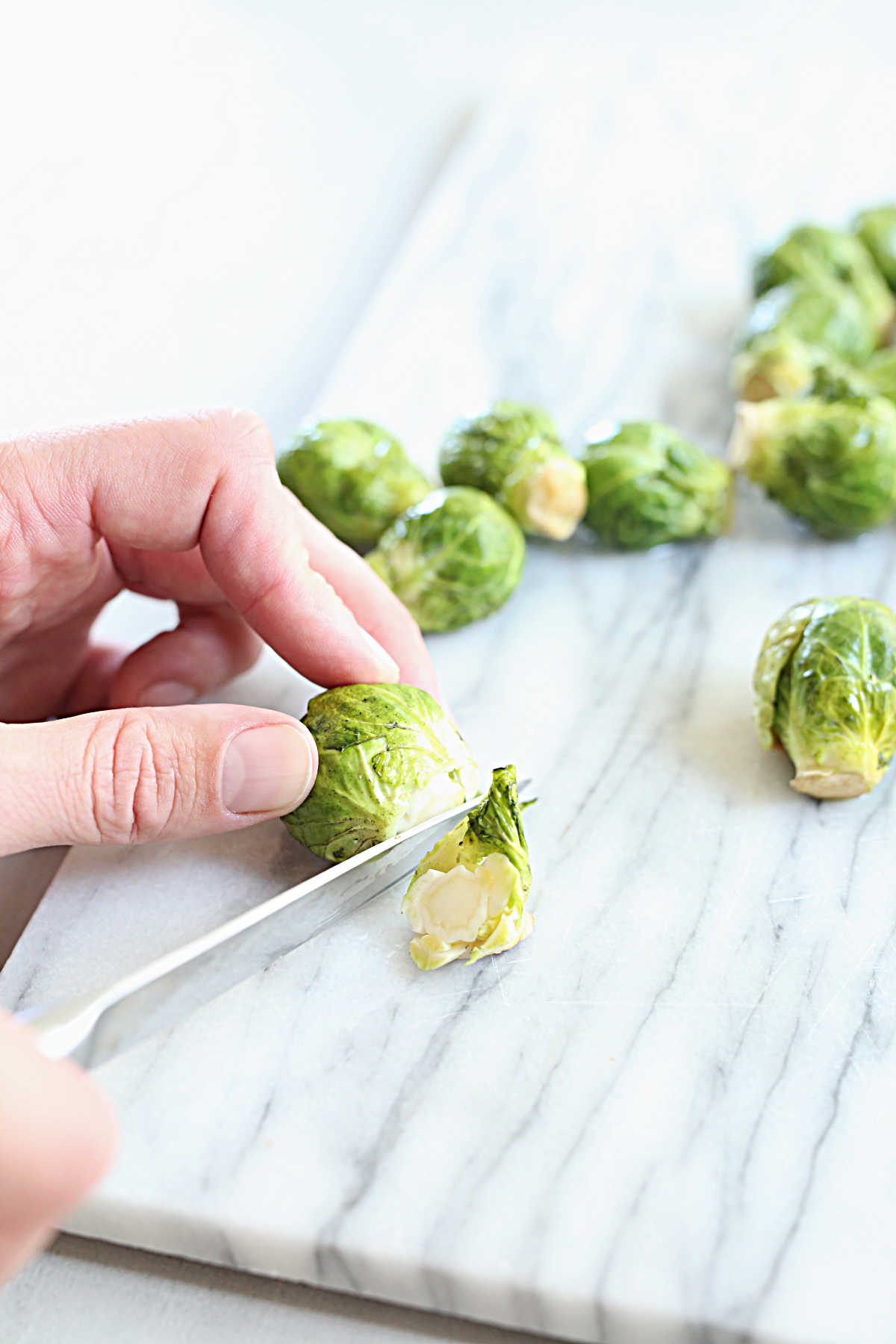 hands holding a knife demonstrating how to cut and trim brussels sprouts from the top to bottom
