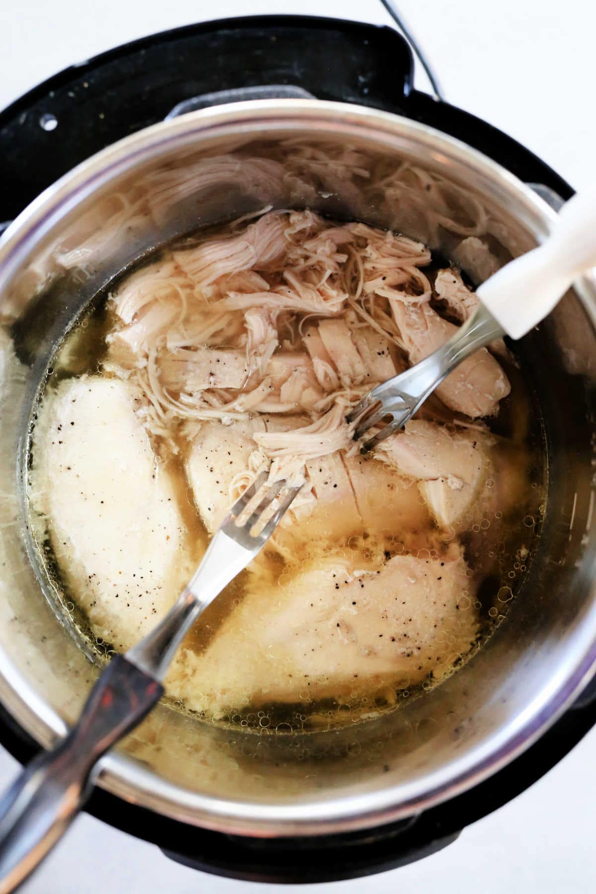 chicken cooked in a slow cooker being pulled apart with forks