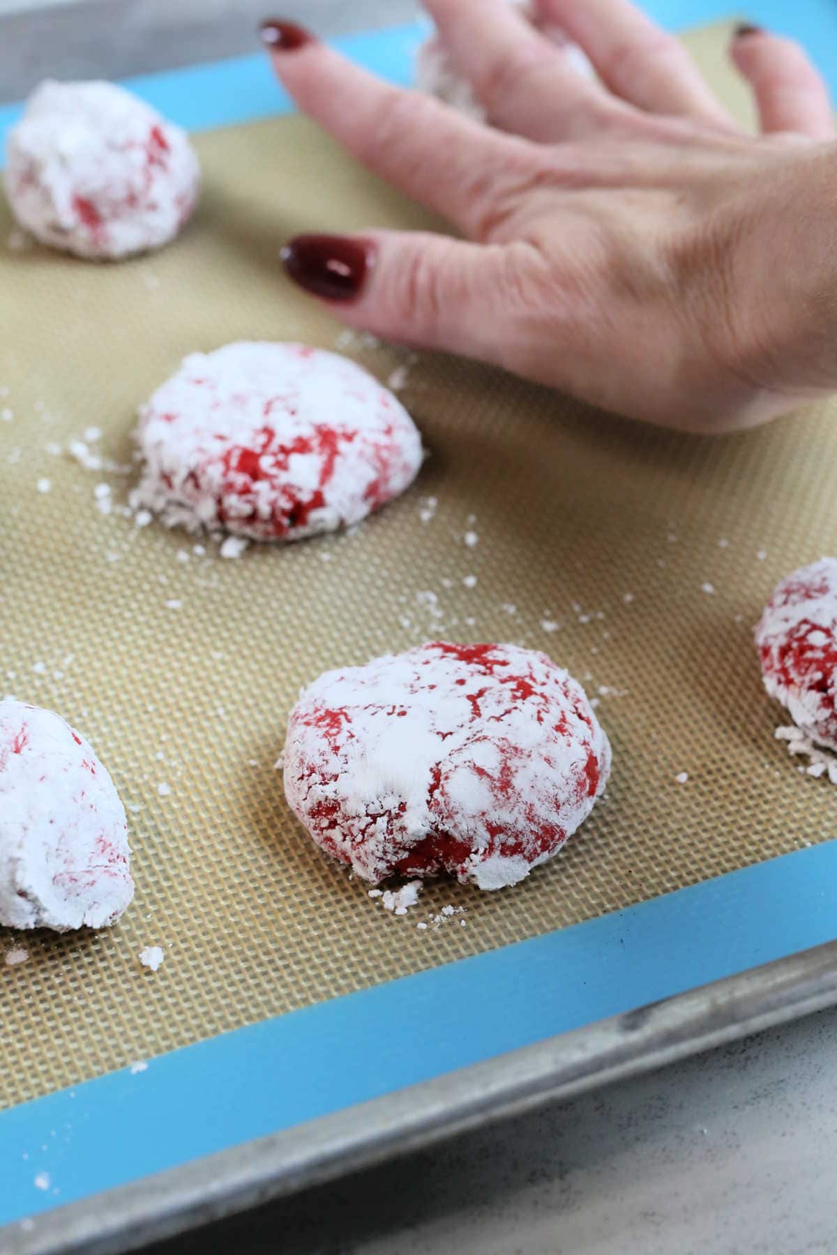 hand pressing down red Christmas crinkle cookie to give it a crackle effect