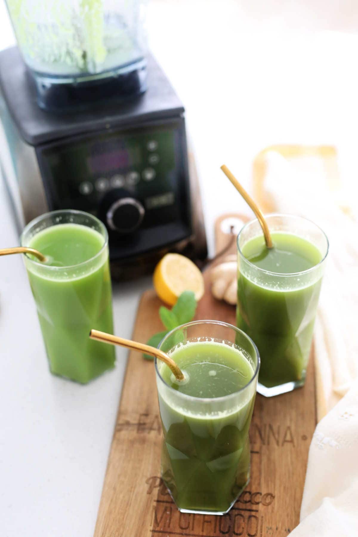 three green detox drinks in glasses with a vitamix