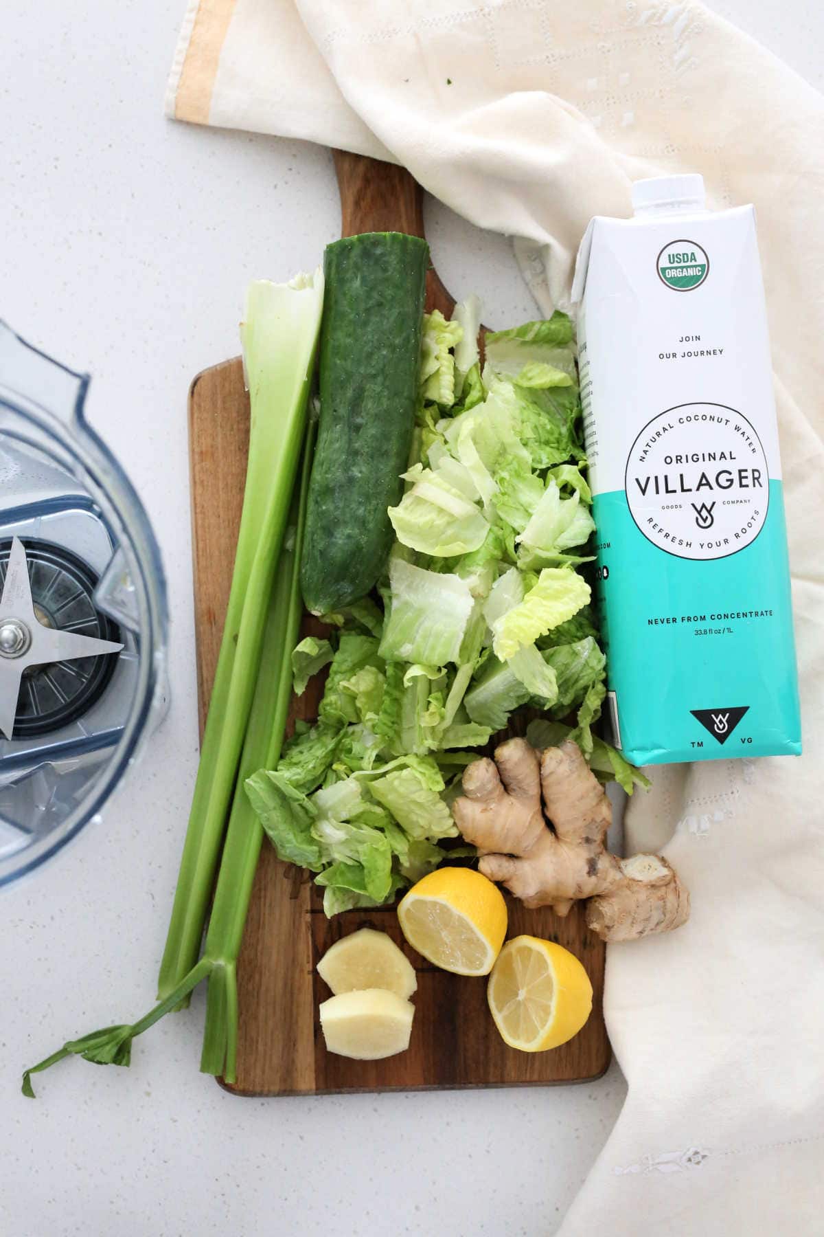 celery, lettuce, ginger, lemon, coconut water ingredients on a cutting board to make a detox green juice drink
