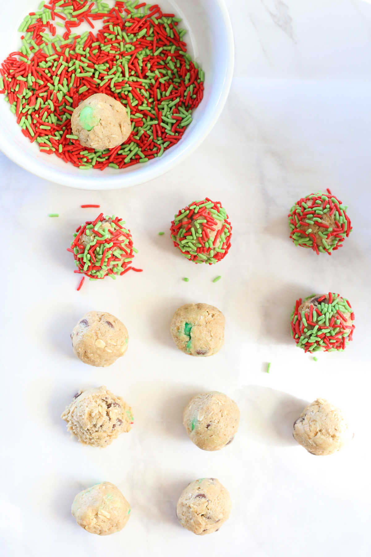 gluten-free christmas cookie dough rolled into balls with a bowl of red and green sprinkles for dipping