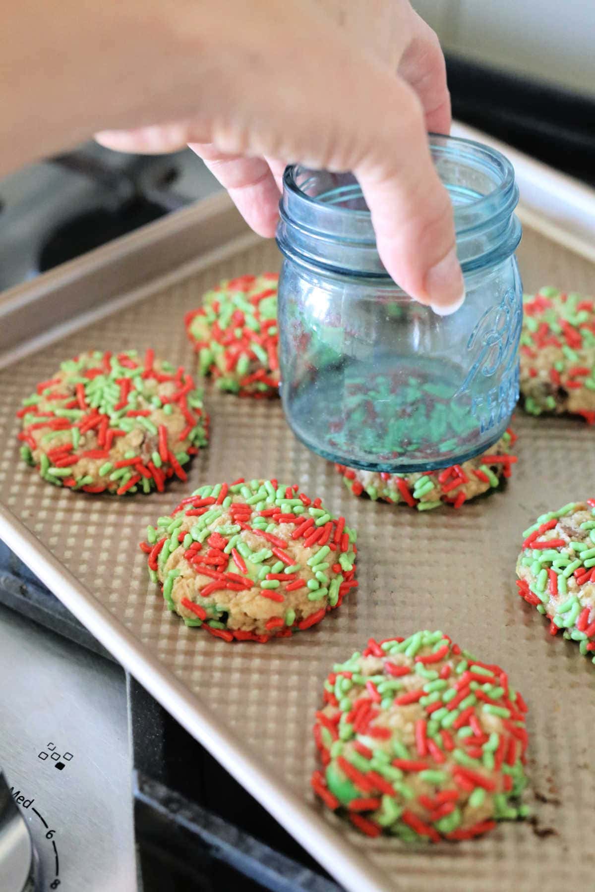 Christmas cookies on a baking pan covered in sprinkles and flatten with cup