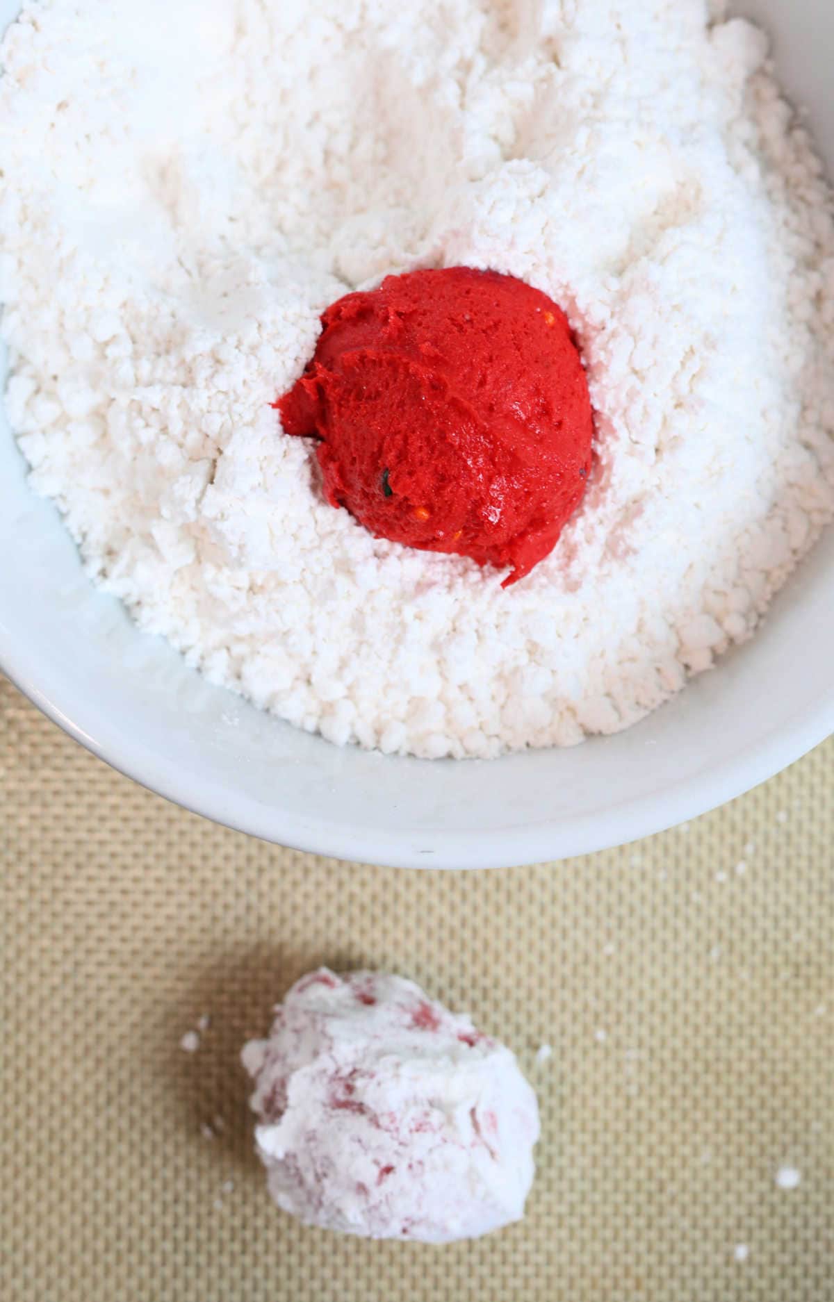 red cookie dough ball in a bowl of confectioners powder sugar