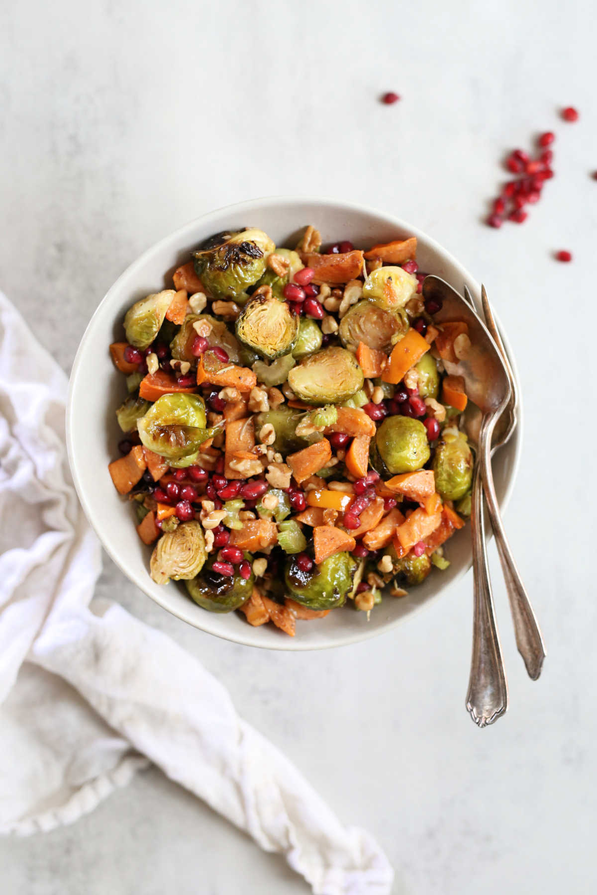roasted brussels sprouts salad recipe in a bowl with serving spoons and a dish towel next to it