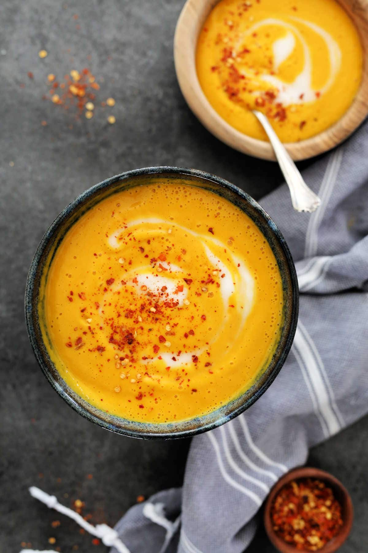 overhead image of easy butternut squash apple soup in a bowl with red pepper flakes and a dish towel