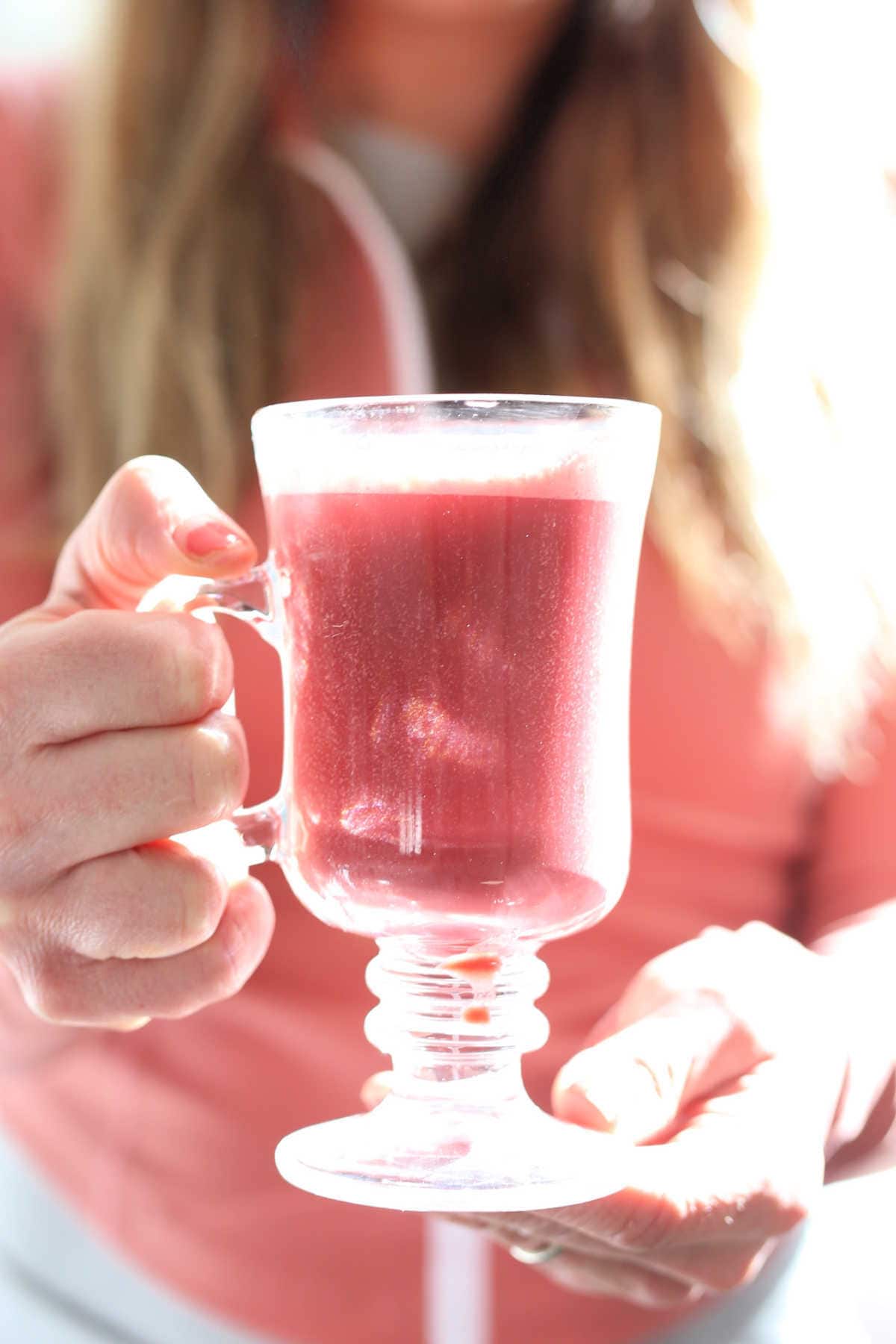 hands holding a pink beet latte in a glass mug