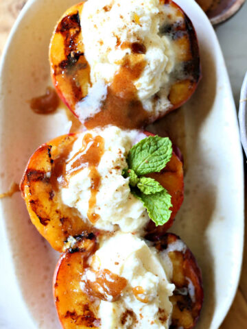 Grilled stuffed peaches and cream recipe with vanilla honey drizzled on top and fresh mint leaves.