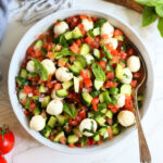 Tomato cucumber caprese salad in a bowl with fresh tomatoes basil and min mozzarella balls.