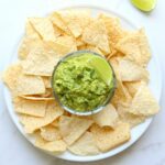 Creamy Guacamole In a Salsa Bowl With a Lime Wedge and Chips on a Plate.