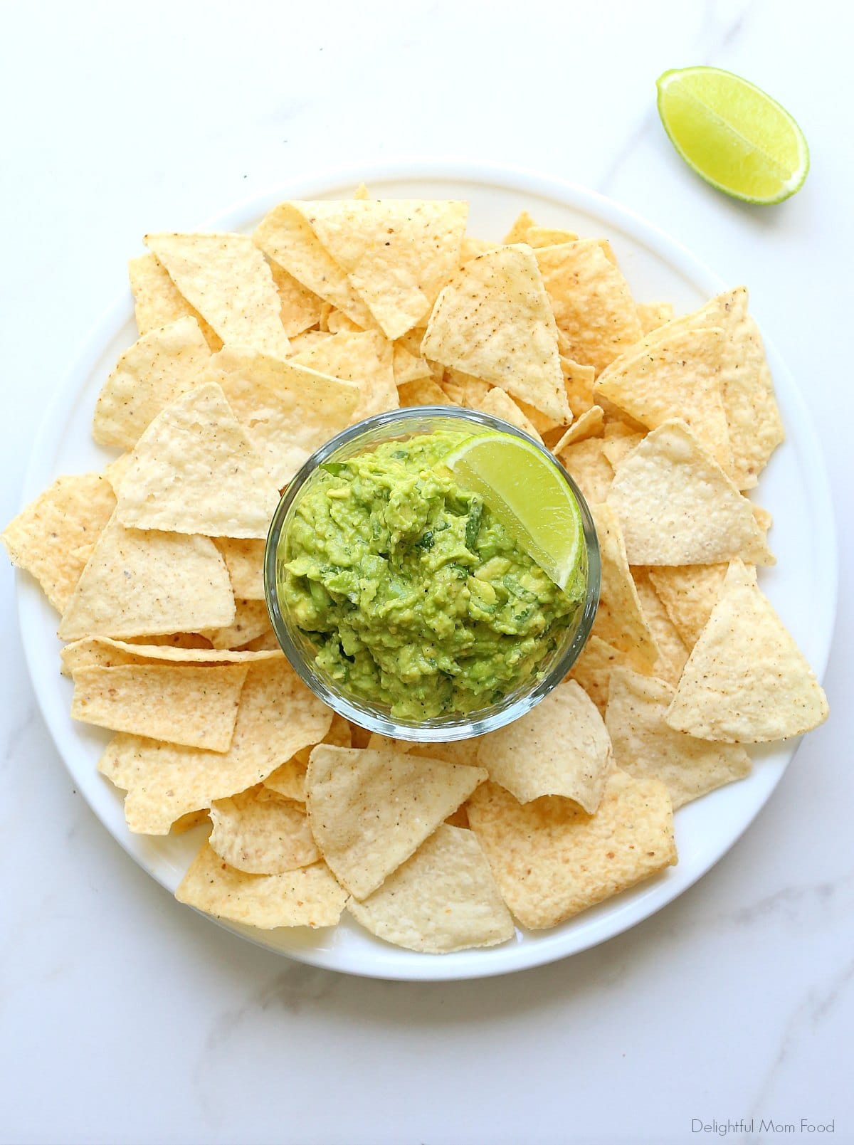 Creamy Guacamole In a Salsa Bowl With a Lime Wedge and Chips on a Plate.