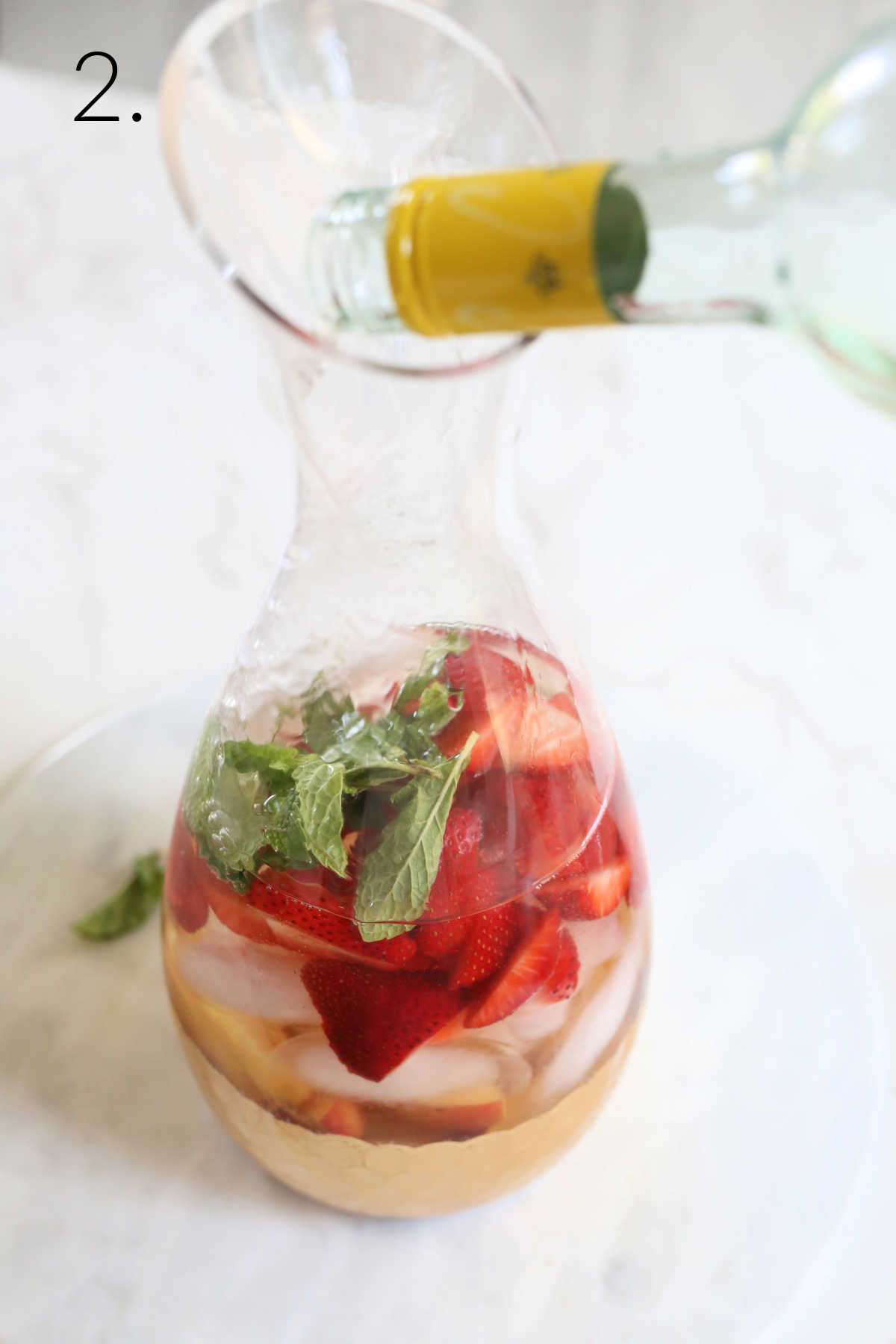 Pouring white wine in a pitcher with peaches and strawberries for sangria.