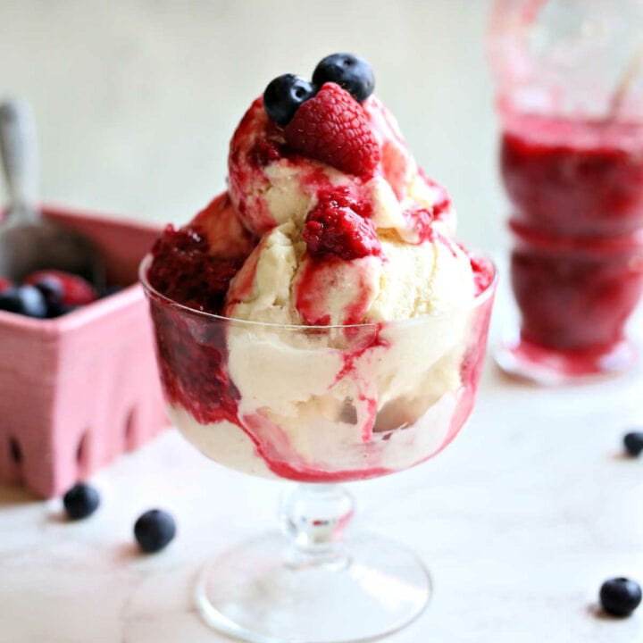 Vanilla coconut milk ice cream in a glass dish drizzled with raspberry sauce and fresh blueberries and raspberries.