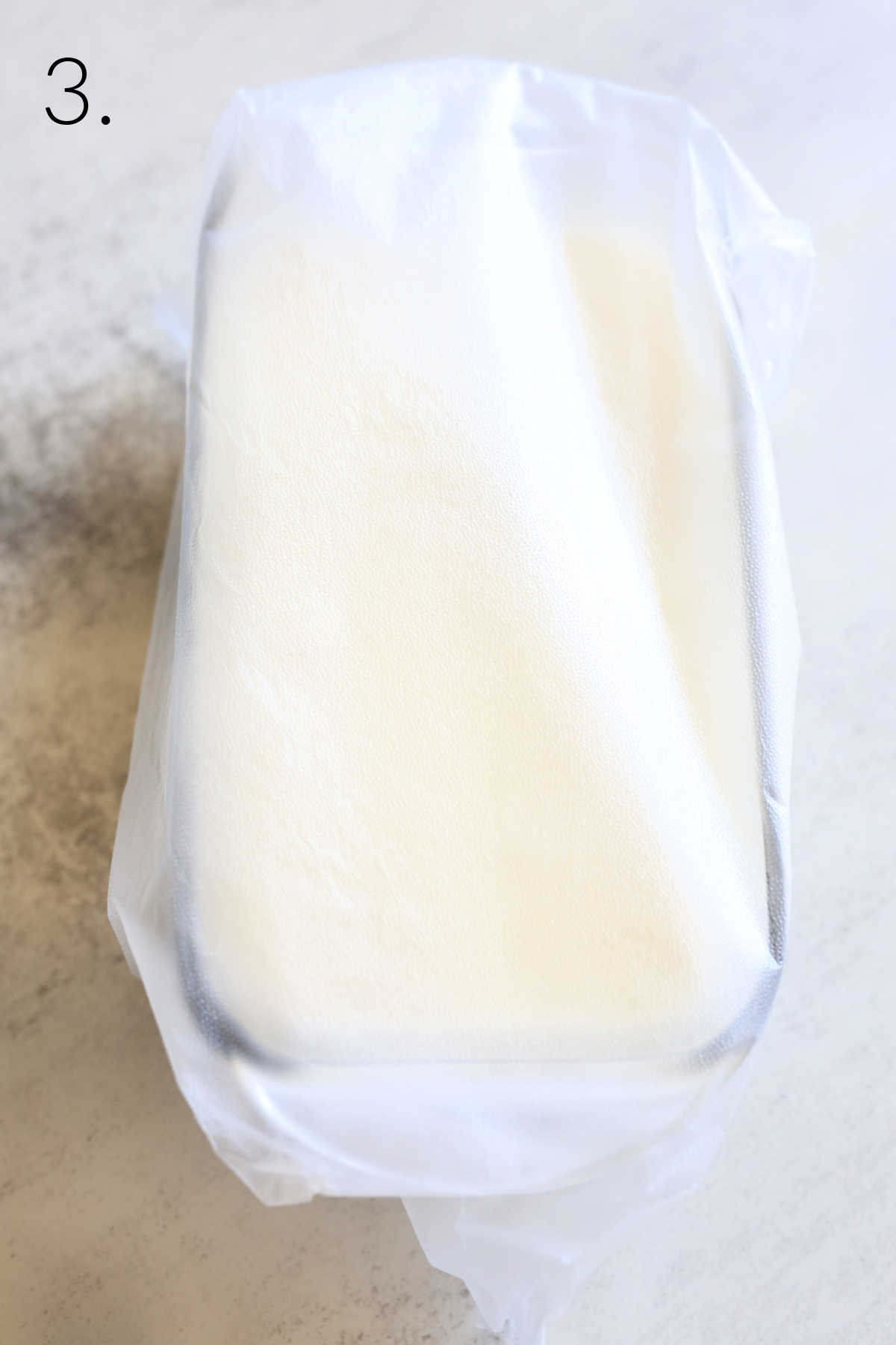 homemade dairy-free ice cream in a glass freezer container with a plastic wrap cover.