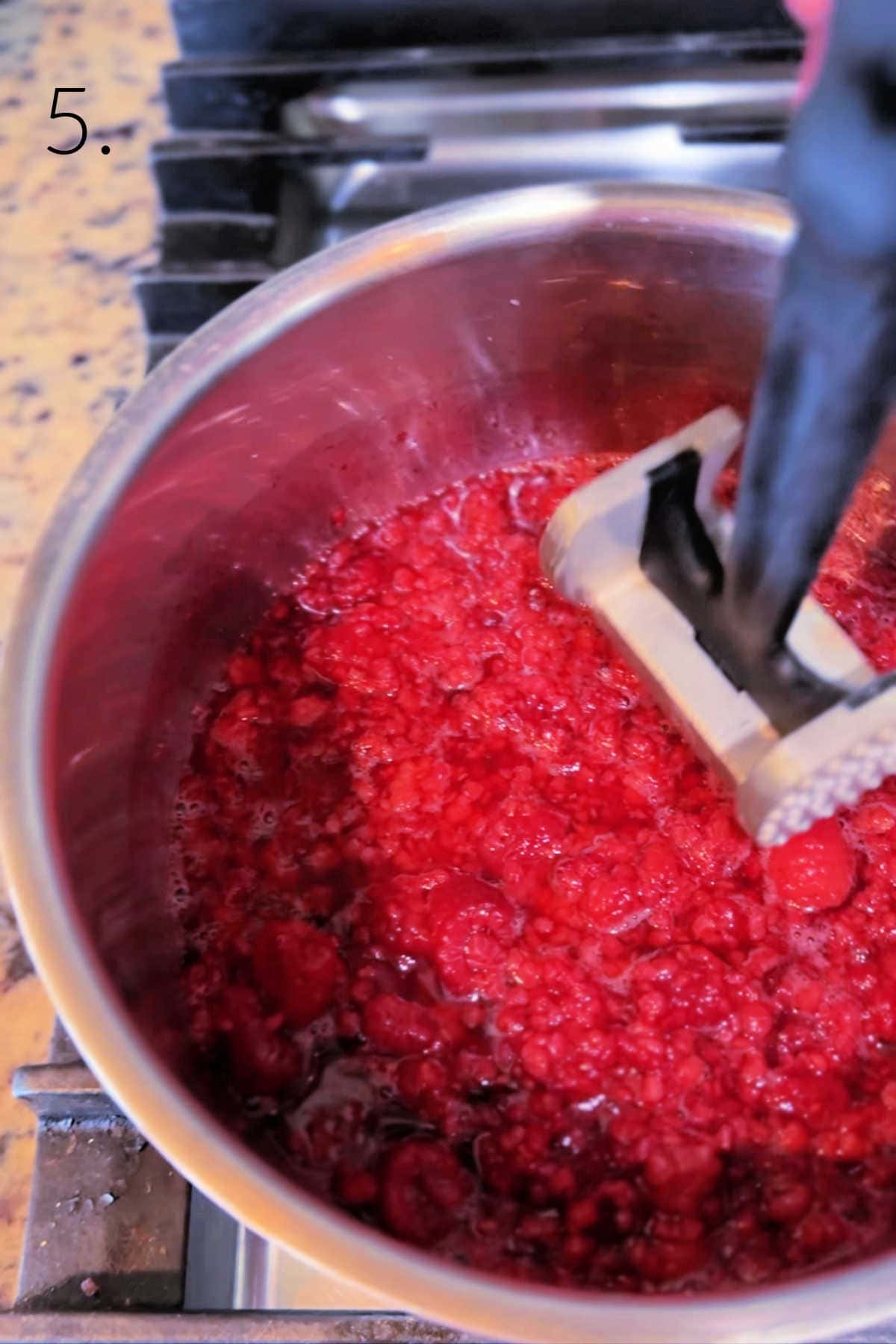 Mashing raspberries in a saucepan for raspberry sauce.
