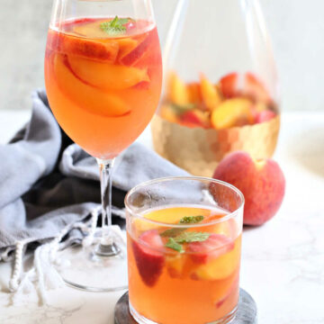 Three glasses of peach sangria white wine and a pitcher with fresh peaches, fruit, and sangria.