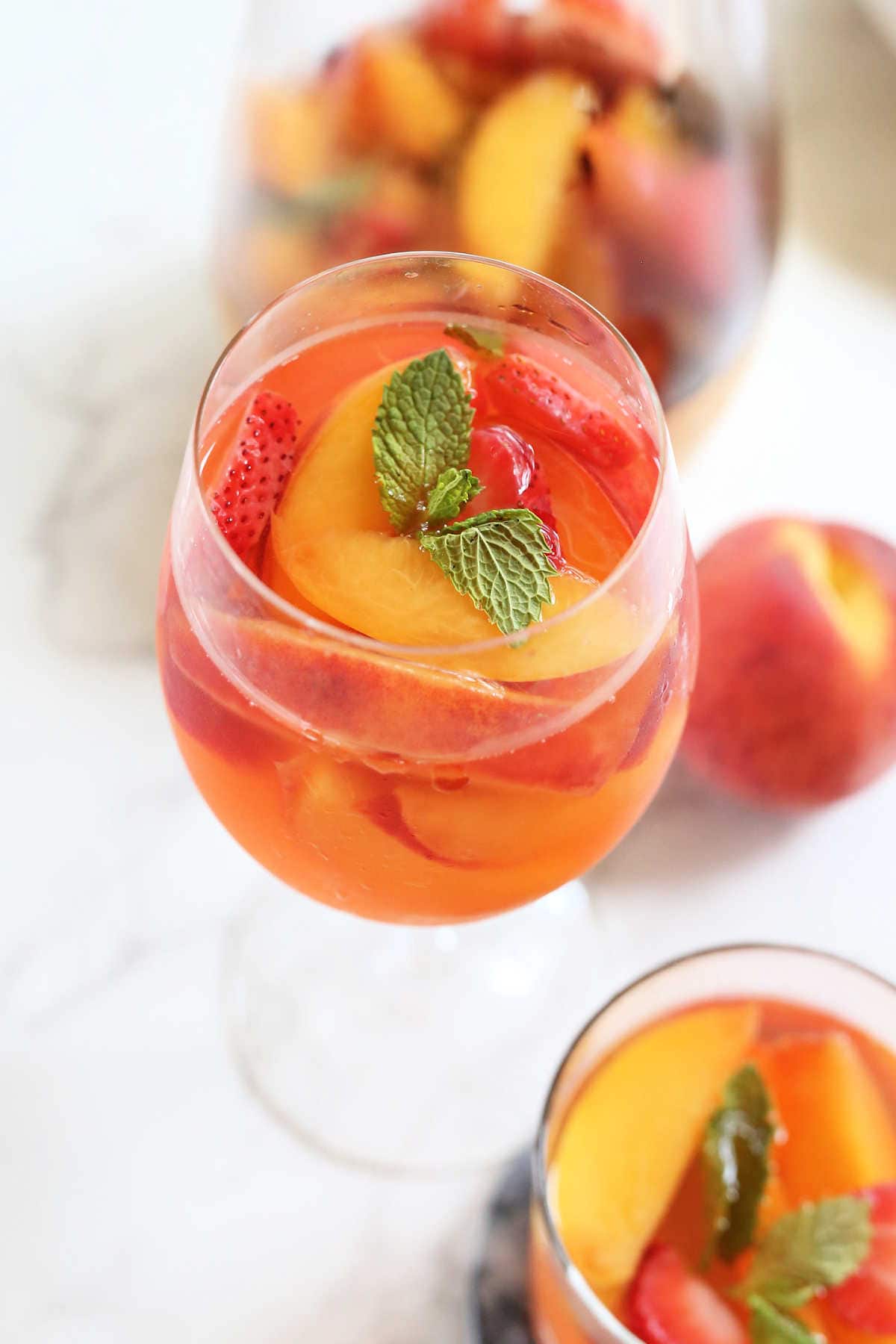Peaches, strawberries, and peach sangria and mint in a wine glass.