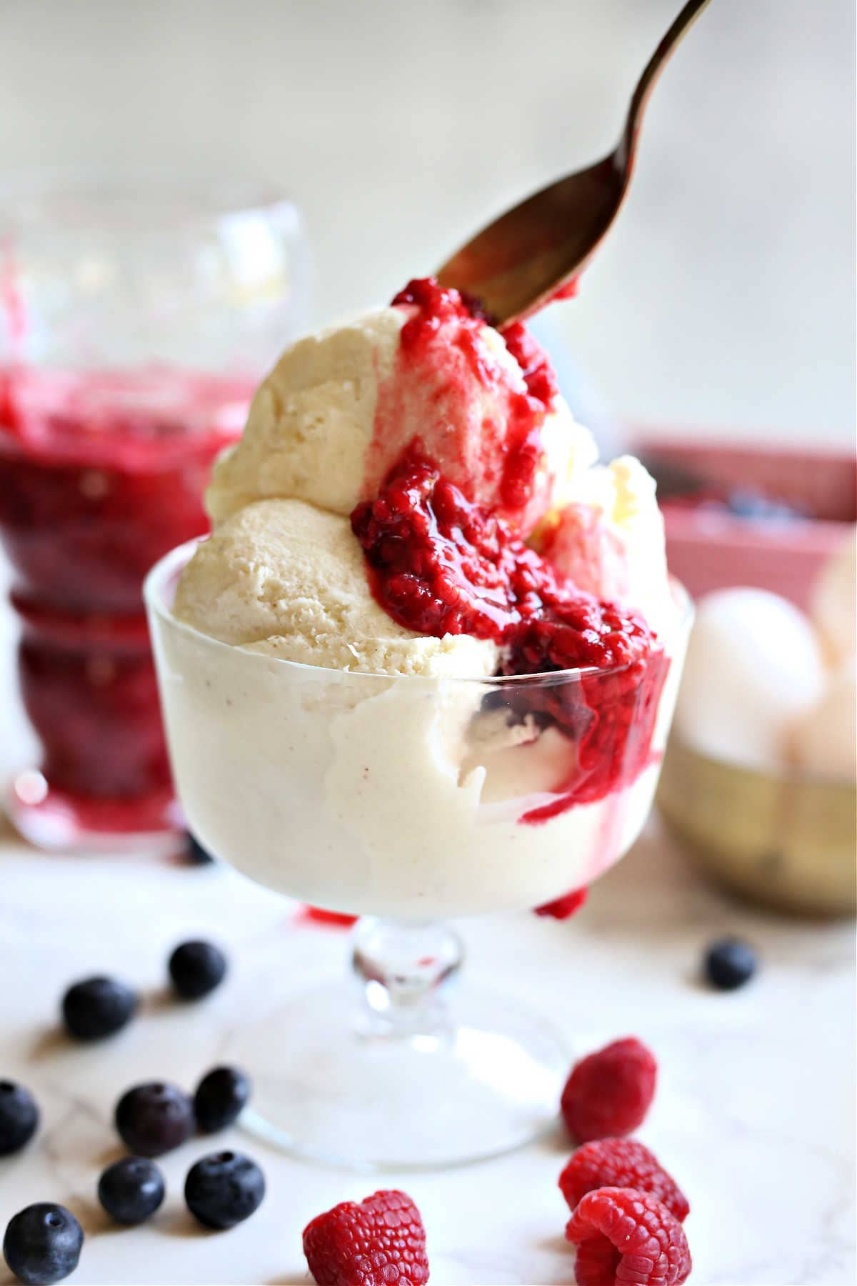 Raspberry sauce drizzled from a spoon on top vanilla coconut milk ice cream.