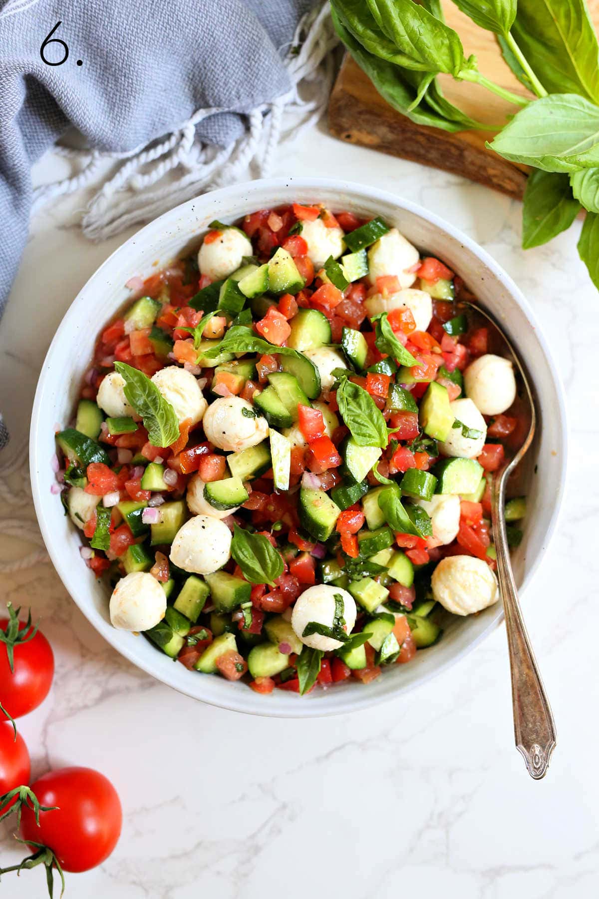 Tomato cucumber mozzarella salad in a bowl with a serving spoon.