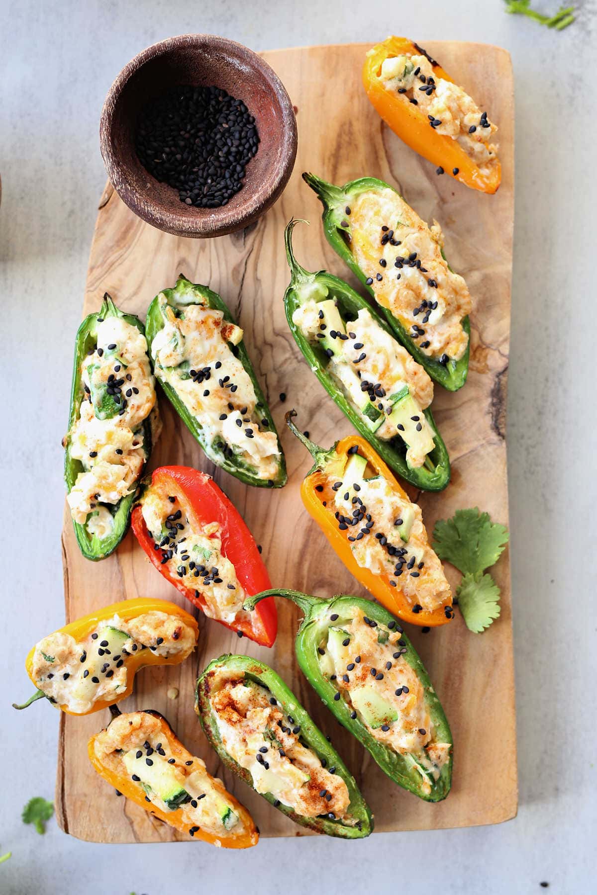 Grilled stuffed jalapenos and mini sweet peppers filled with cream cheese on a wood appetizer board.