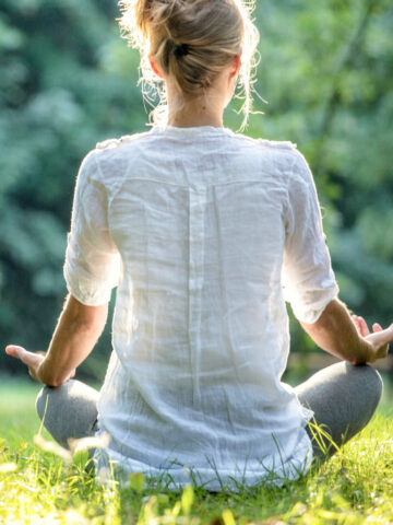 Woman meditating in grass outdoors with hands out.