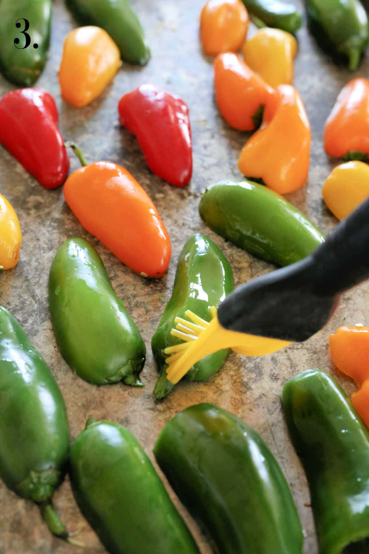 Basting jalapenos and sweet mini peppers with olive oil.