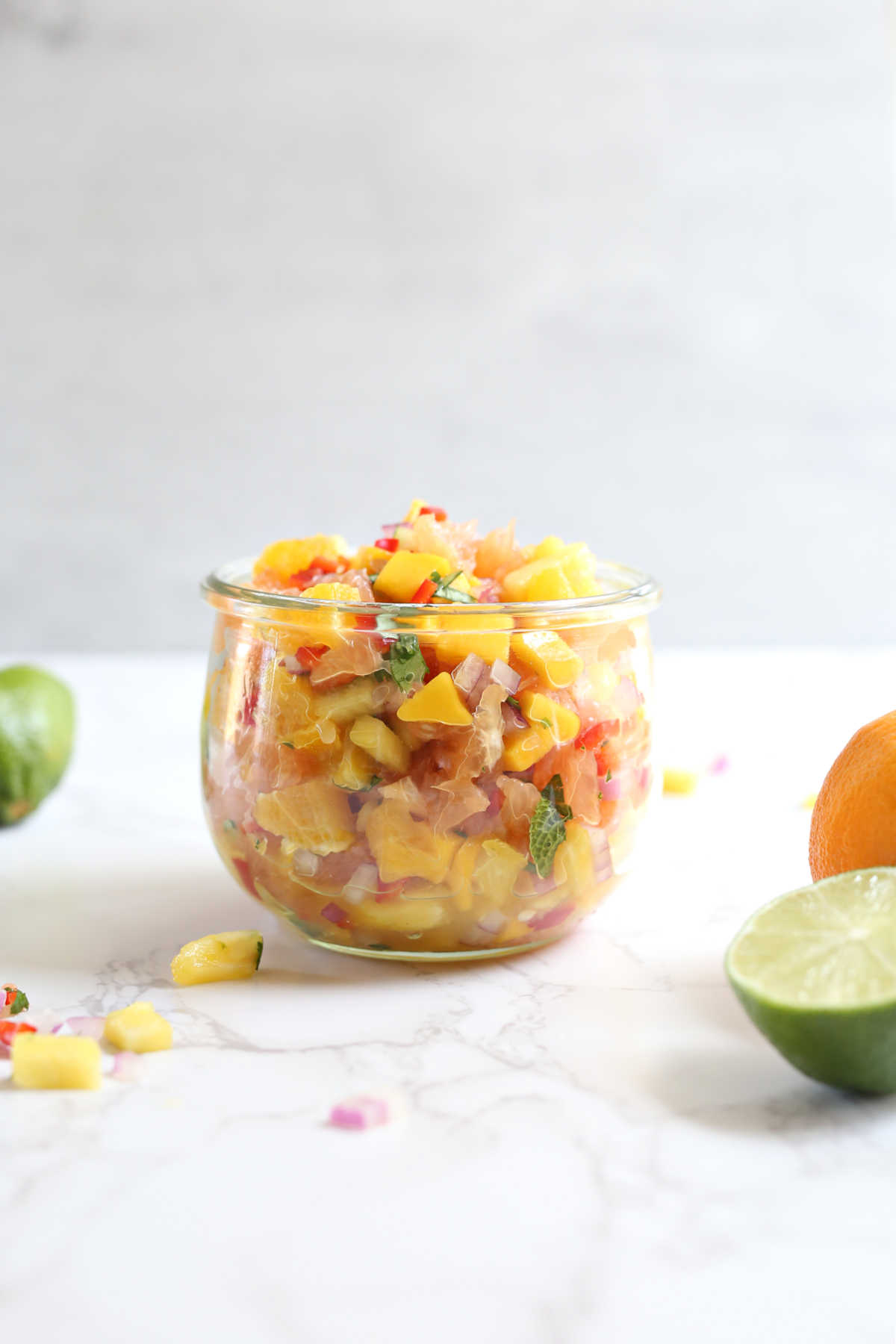 Orange salsa recipe in a glass jar with citrus fruit.