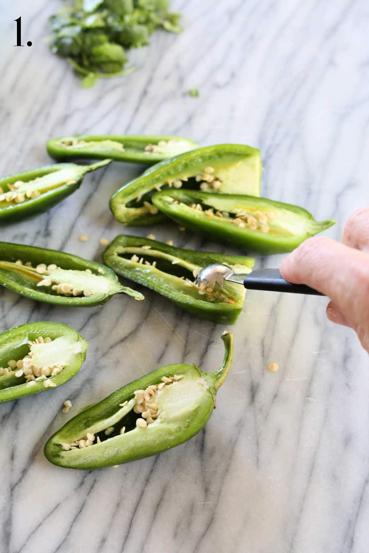 Jalapeno halves with hand scooping out the seeds.