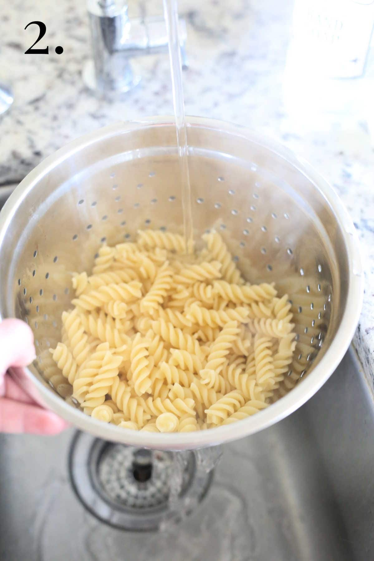 Rinsing cooked pasta noodles with cold water in the sink.