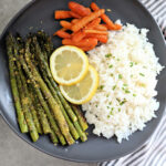Roasted asparagus carrots and rice on a dish with fresh lemon slice.