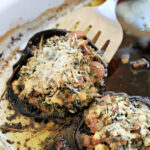 Spatula lifting up portobello mushroom stuffed with sausage and spinach and topped with cheese.