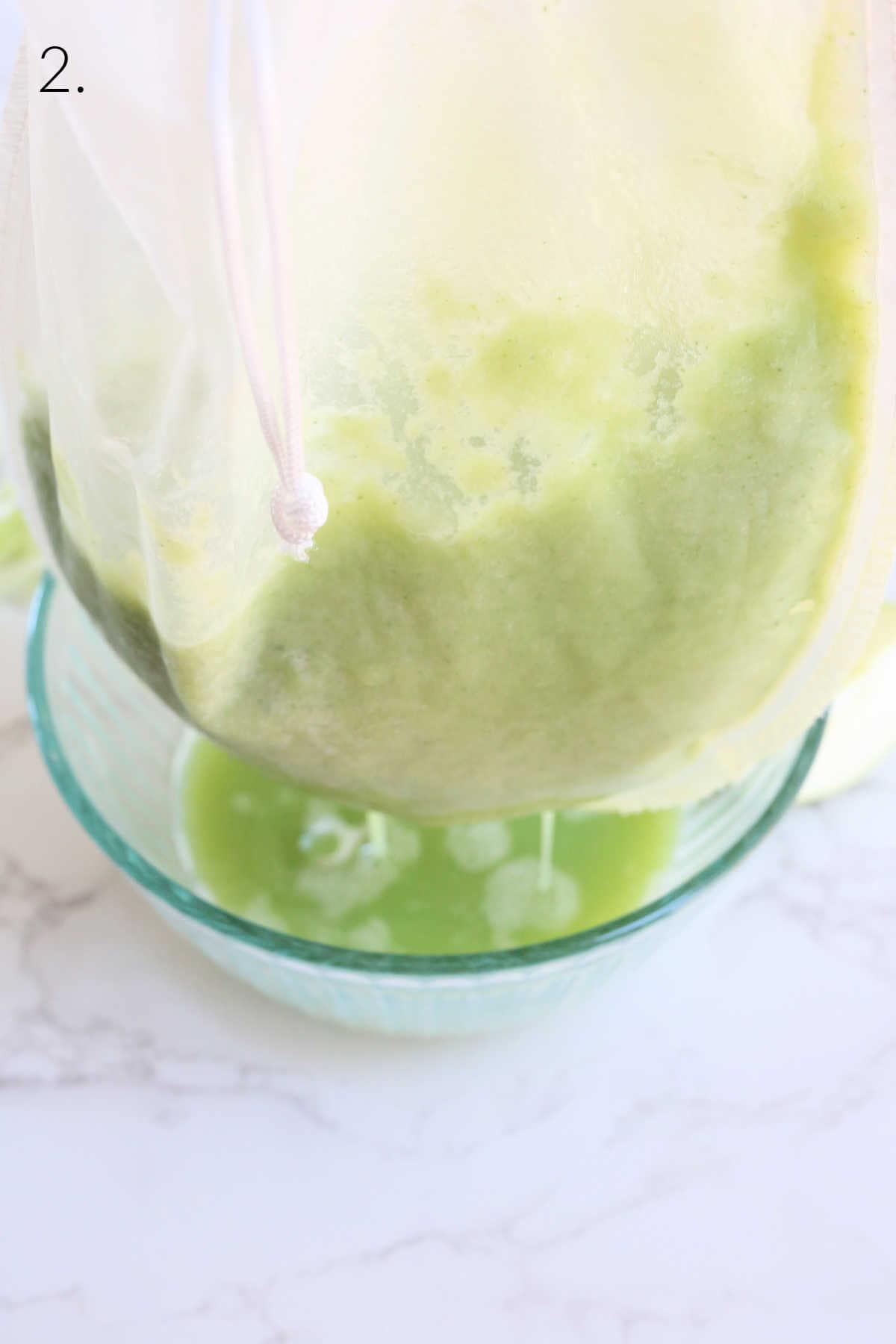 Homemade green juice in a blender squeezing out of a nut bag into a glass bowl.