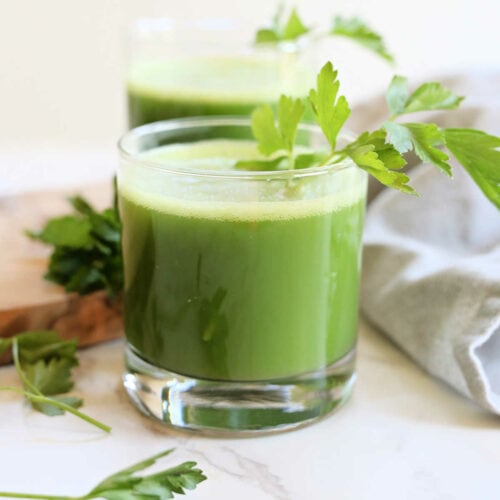 Parsley juice in a glass with parsley leaf and stem as a drink garnish.