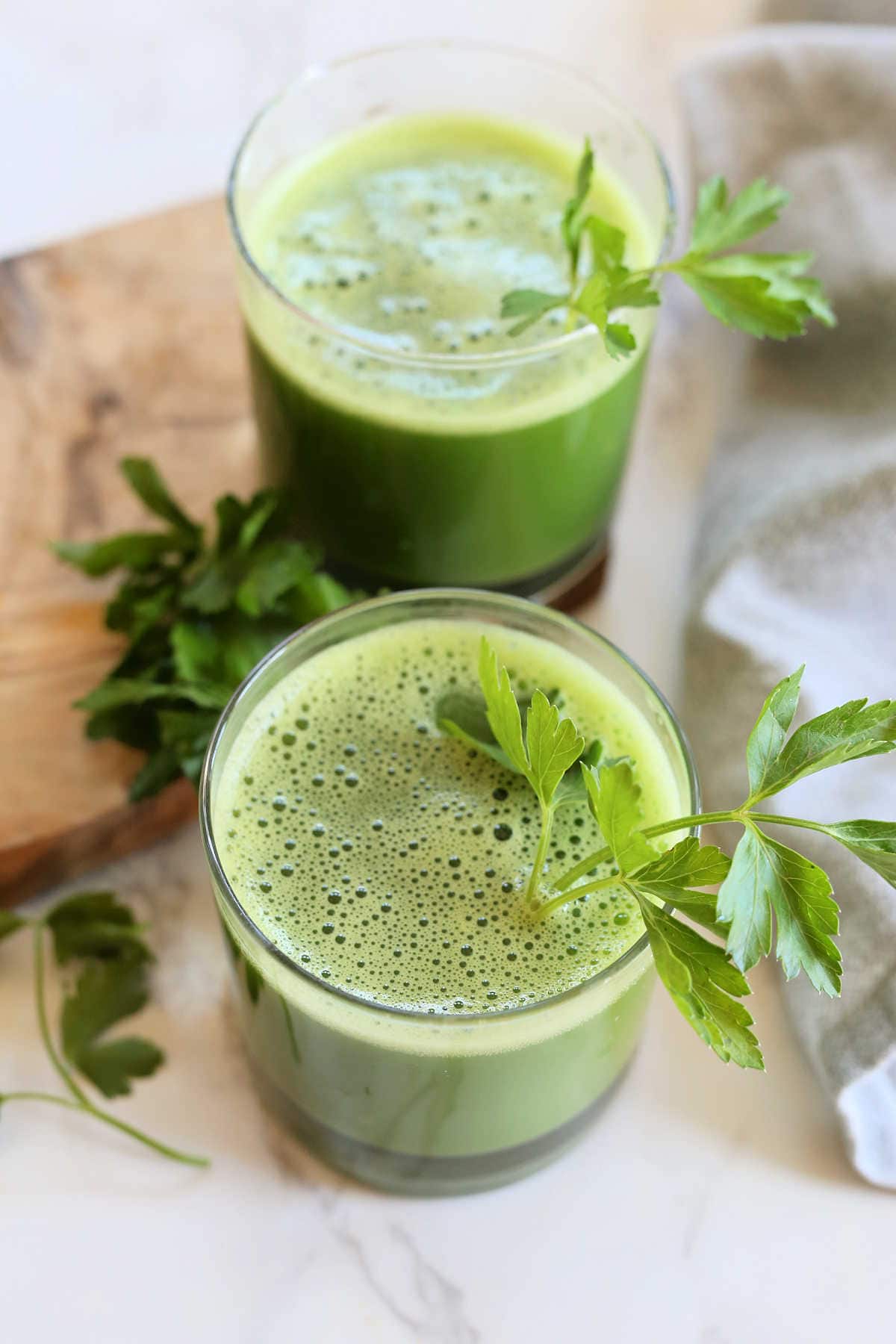Parsley juice with celery and cucumber in two glasses garnished with flat parsley leaves on stem.