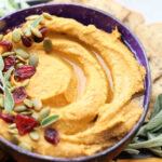 Hummus in a bowl topped with pumpkin seeds and dried cranberries.