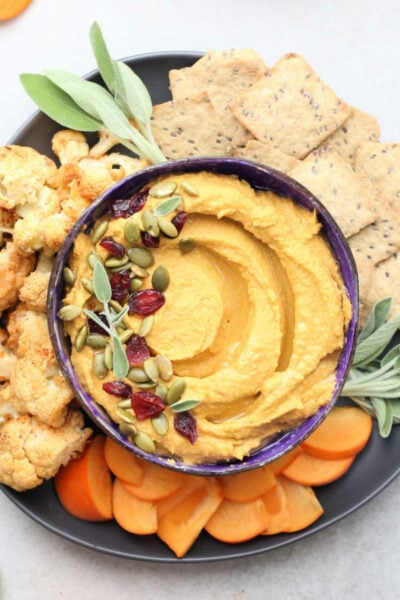 Pumpkin hummus appetizer dip recipe in a bowl with fruit and vegetables.