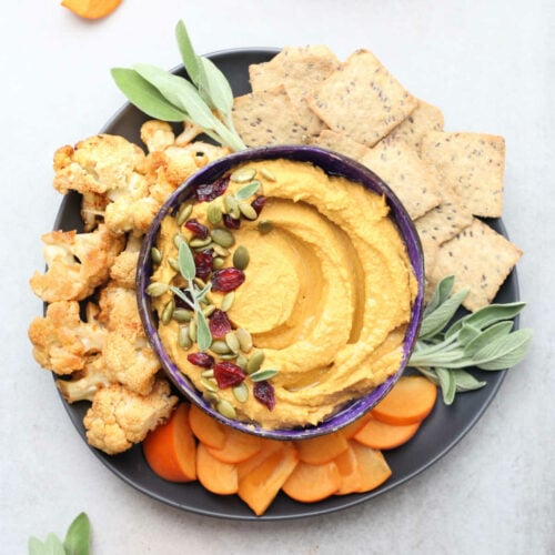 Pumpkin hummus appetizer dip recipe in a bowl with fruit and vegetables.