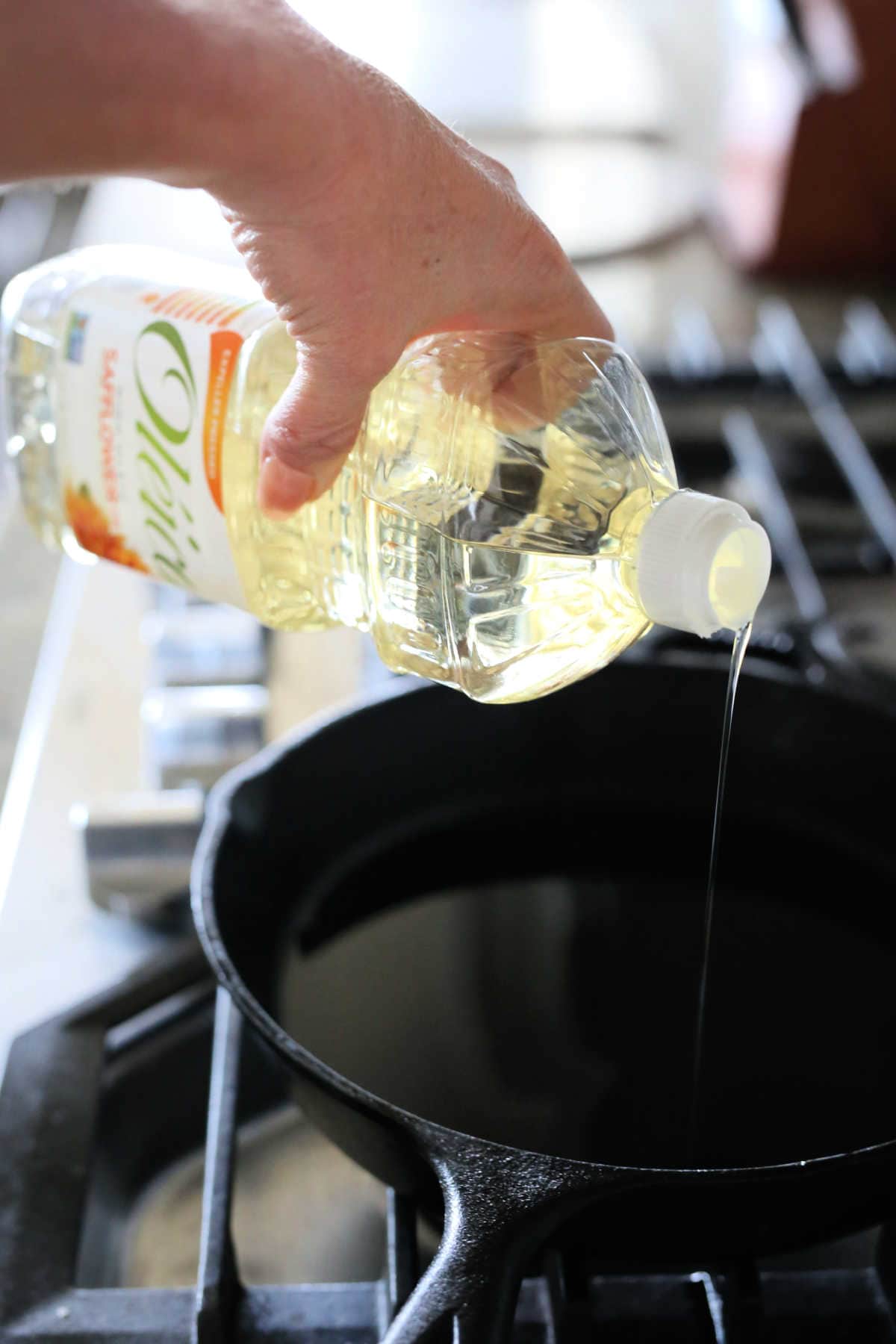 Hand pouring oil for frying in a cast iron skillet.