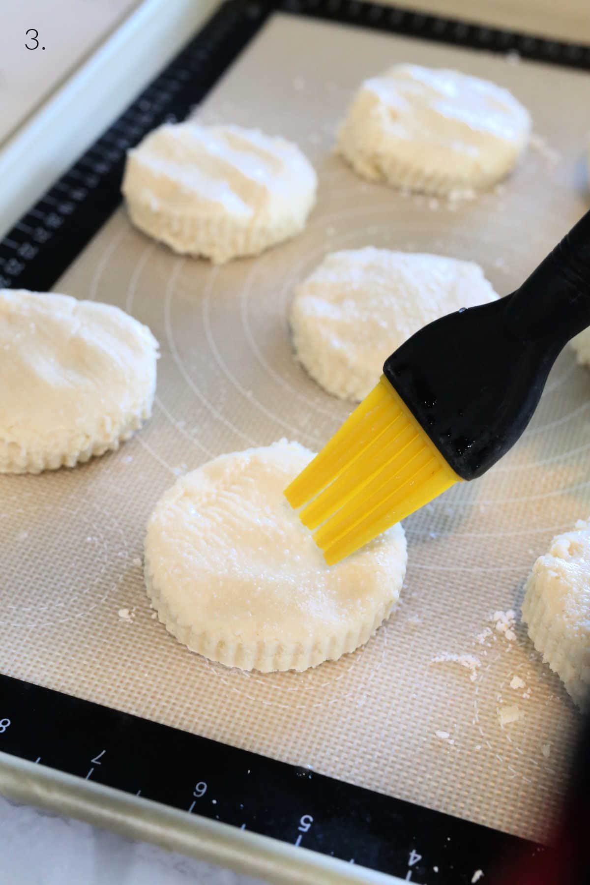Brushing the tops of gluten and dairy-free biscuits with water using a basting brush.