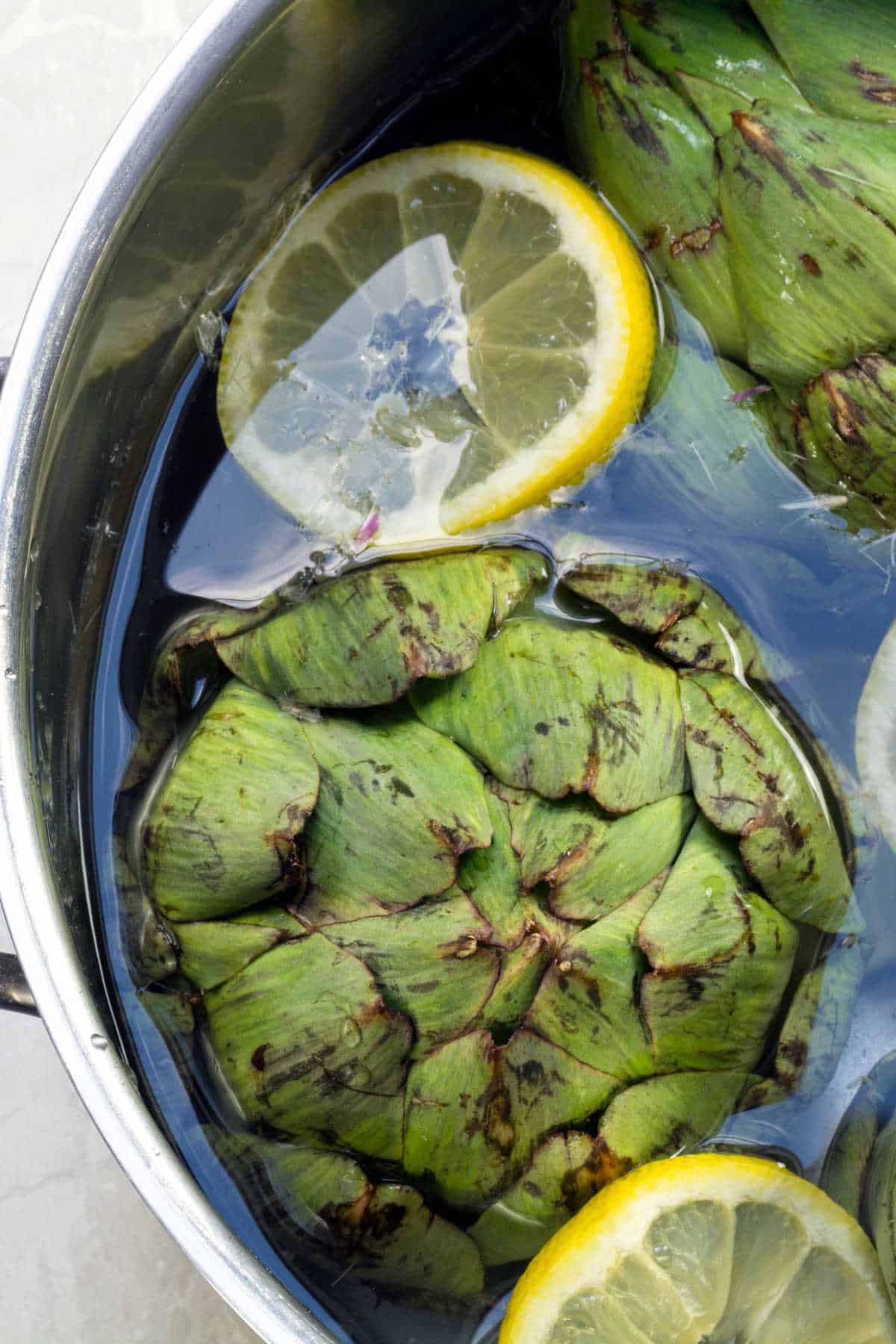 Artichoke vegetables and lemon slice in a pot of water.