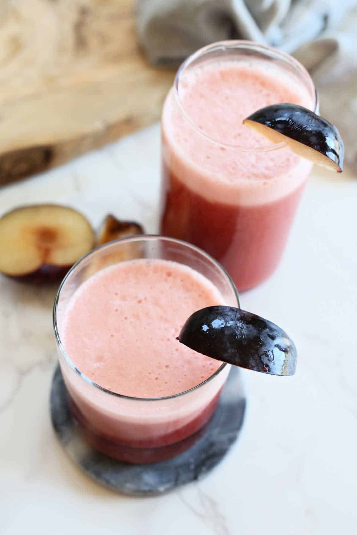 Two glasses of fresh plum juice garnished with plum slices.