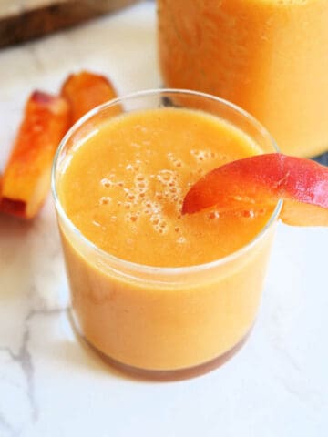 Peach nectar in a glass with a peach slice.