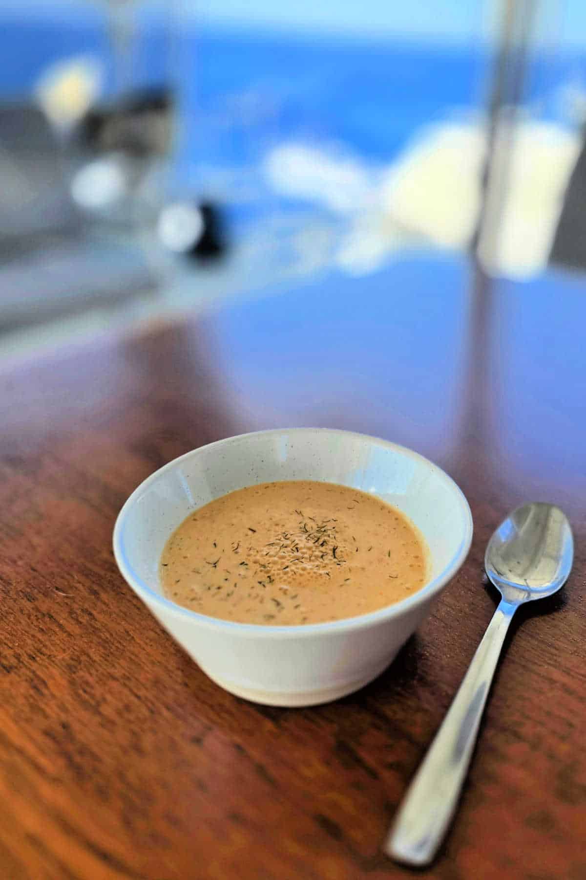 Cucumber gazpacho soup recipe in a bowl with a spoon by the sea.