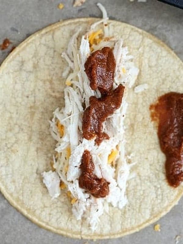 Corn tortilla topped with shredded chicken, cheese and enchilada sauce ready to roll.