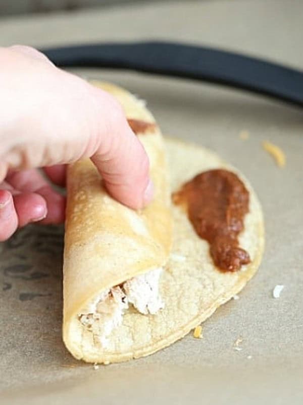 Hands rolling up a filled corn tortilla for chicken enchiladas.